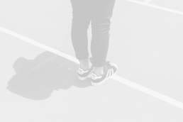 A pair of Adidas sneakers worn by a person standing on a track, showcasing athletic footwear with a stylish design.